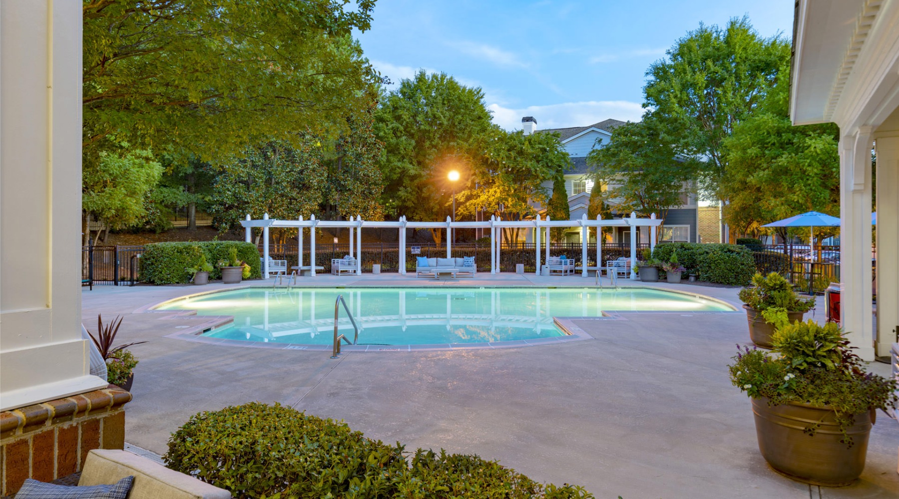 resort style pool with seating and trees in the background at dusk
