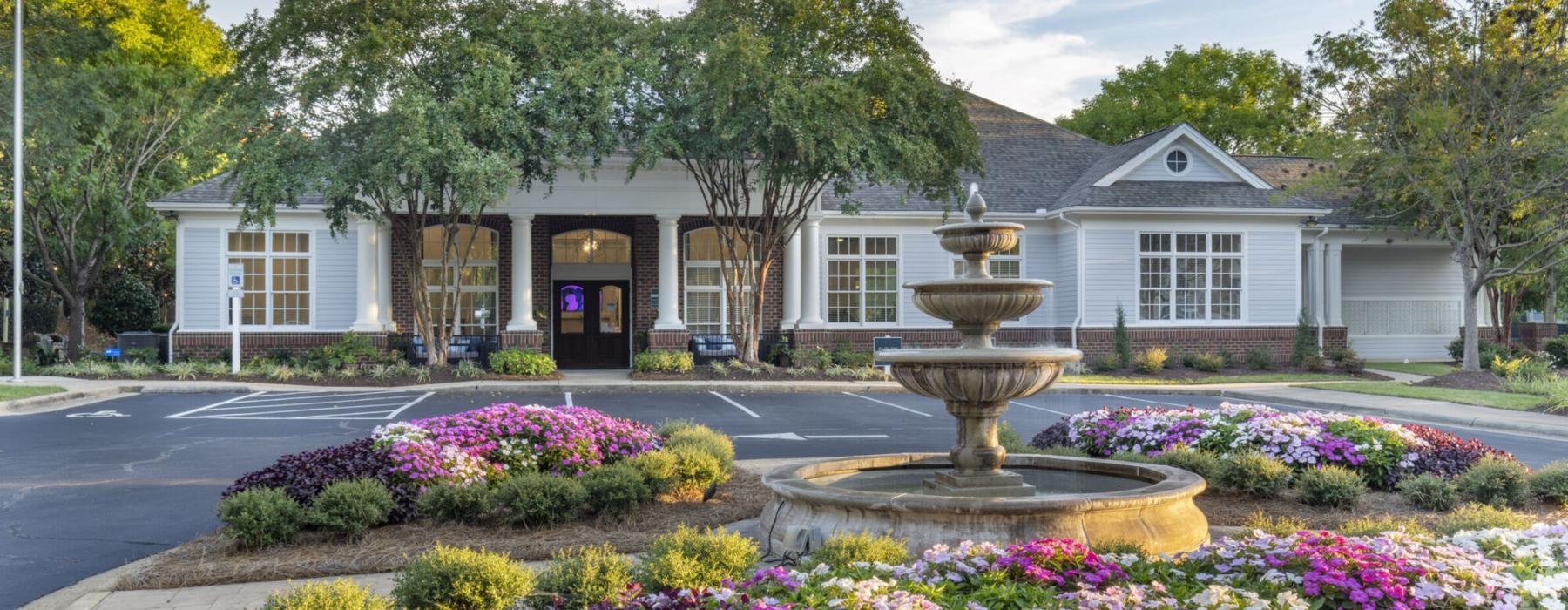 a fountain in front with flowers of a building